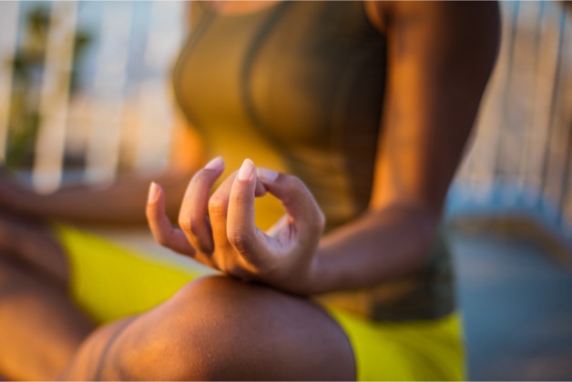 Close up on the hand of a young black woman in nature sitting in a yoga position.