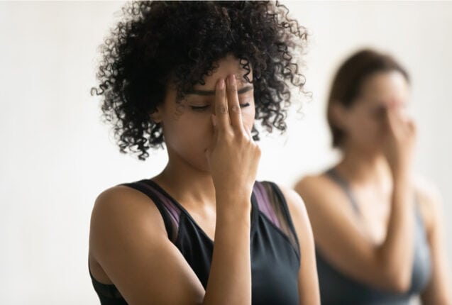 During yoga class women do Alternate Nostril breathing, close up focus on a black woman.