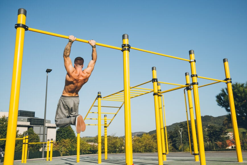 Young athletic man doing gymnastics on bars at a calisthenics gym outdoors.