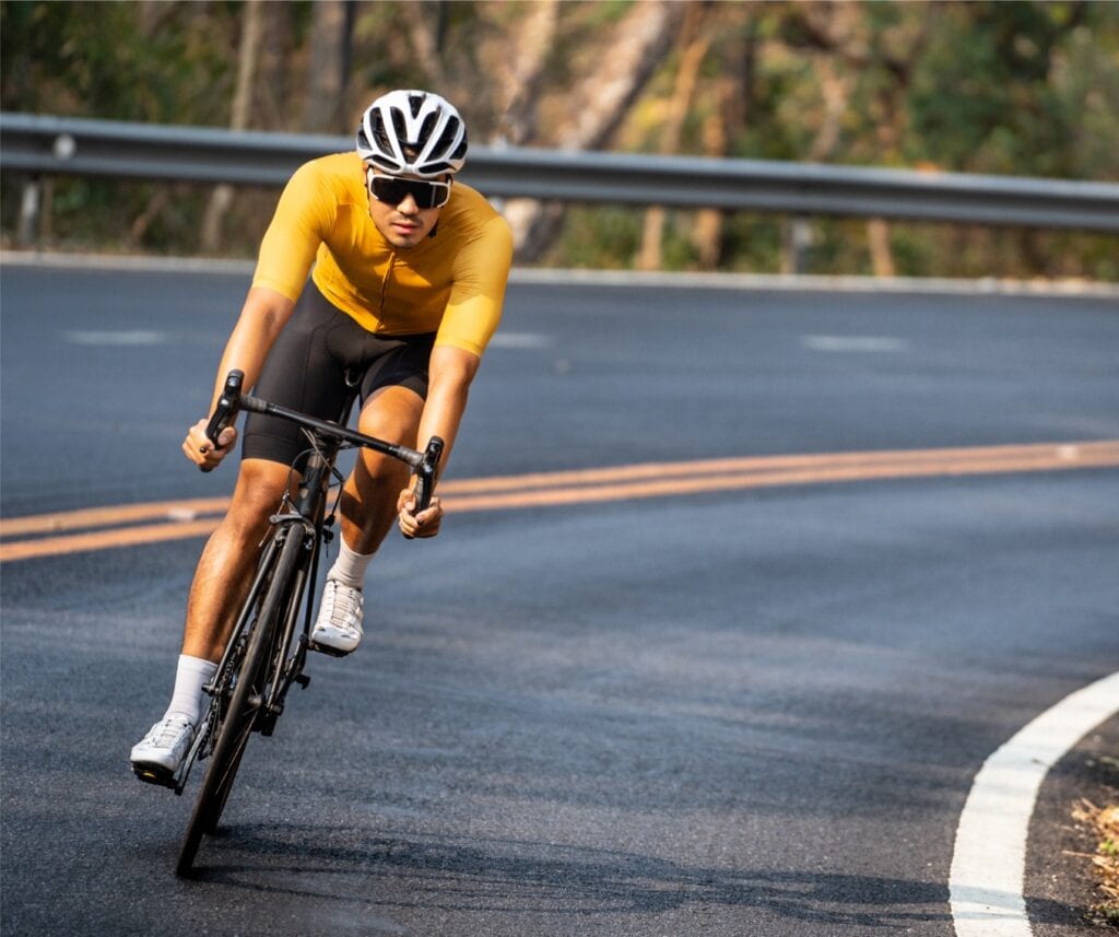 Man in yellow cycling jersey riding on road bike with willful face.
