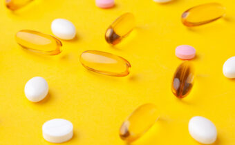 Many scattered vitamins, pills, softgels, and tablets on a yellow background.
