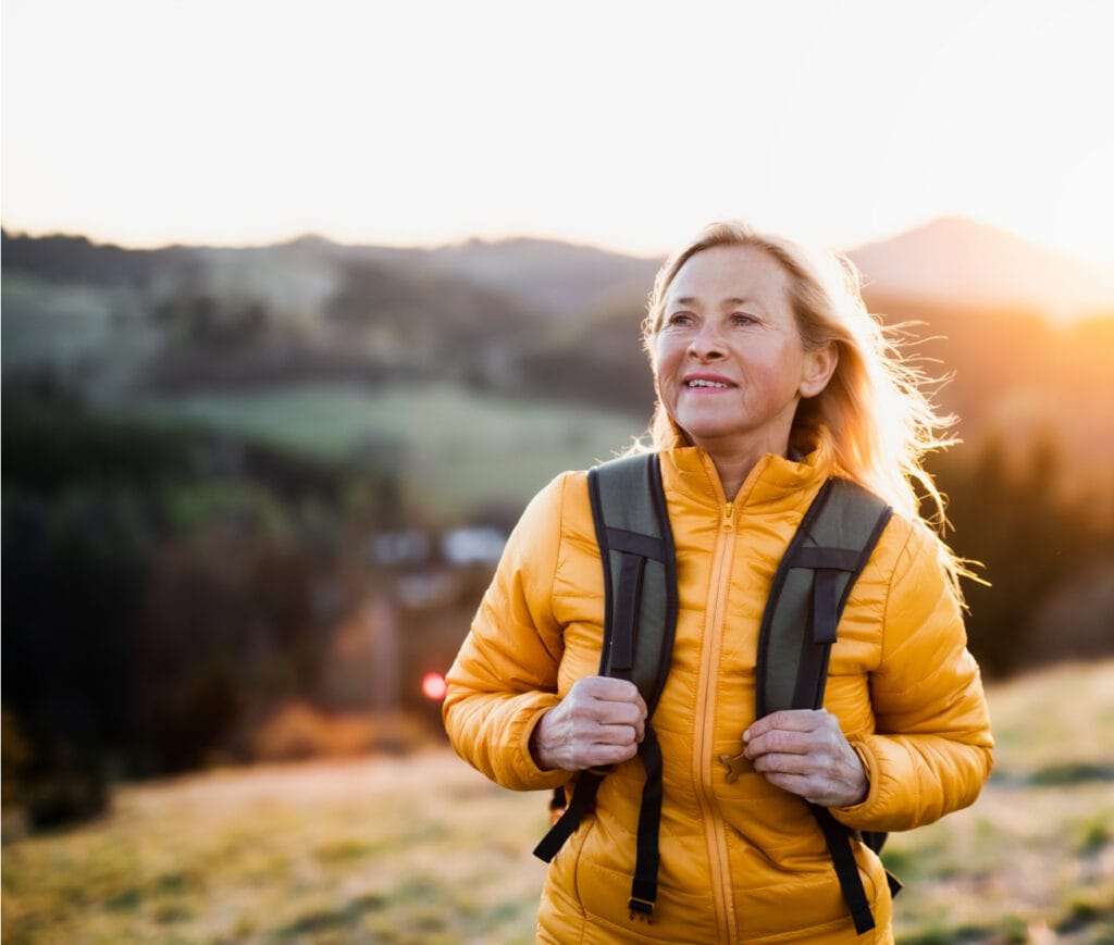 Senior caucasian woman walking outdoors in nature at sunset, hiking.