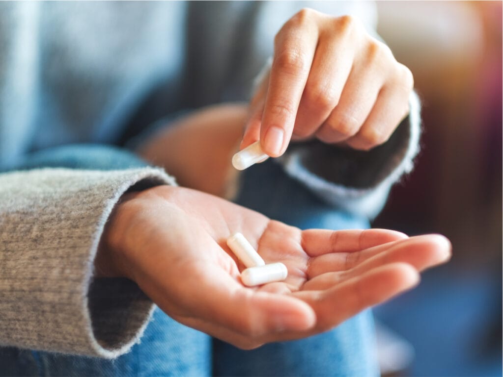 Close up of hands holding white capsules.