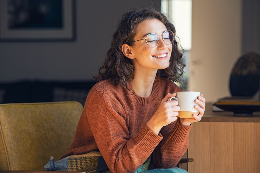 Happy young woman in sweater drinking a cup of tea on an autumn morning.