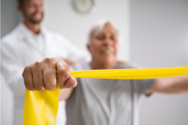 Older, male physical therapy patient using physiotherapy bands for rehabilitation.