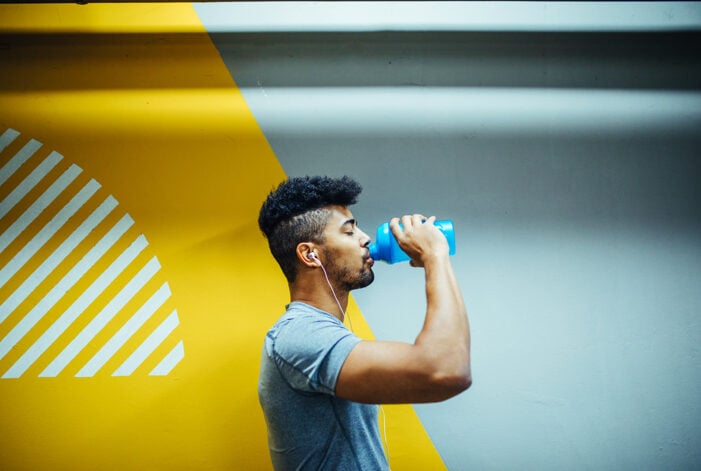 Young athlete taking a break from his training, drinking from a blue water bottle.