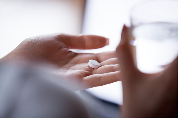 Close up of hand holding pill and glass of water.