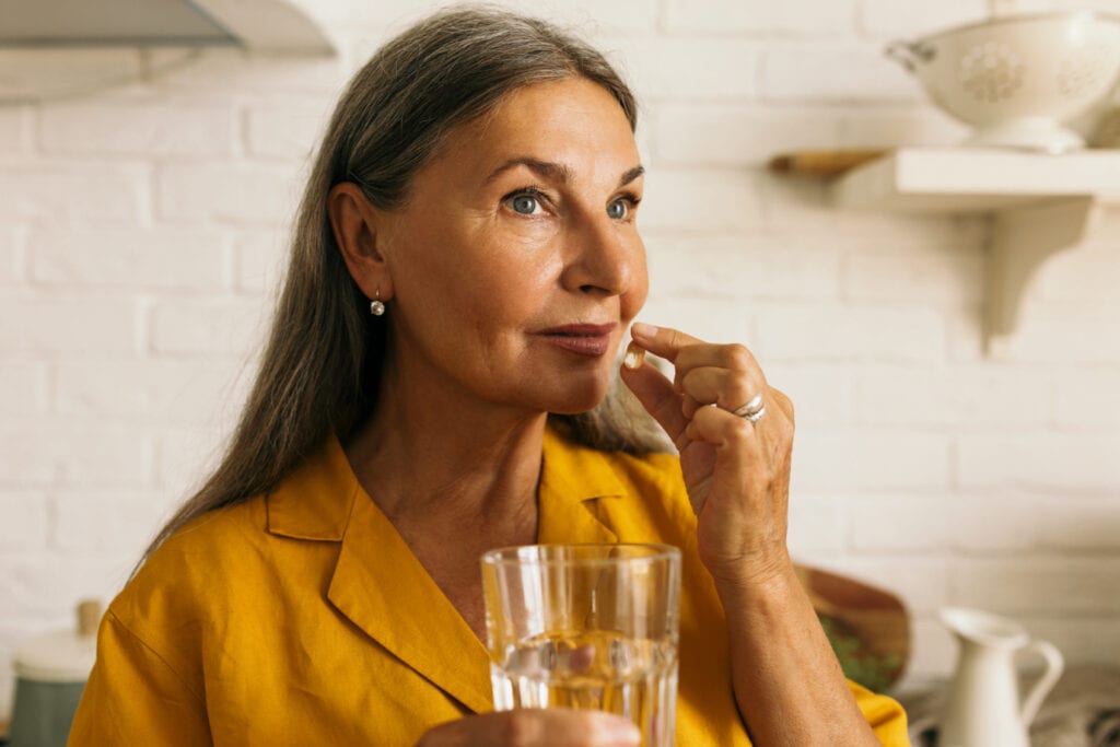 Mature female holding pill to mouth and glass of water in hands.